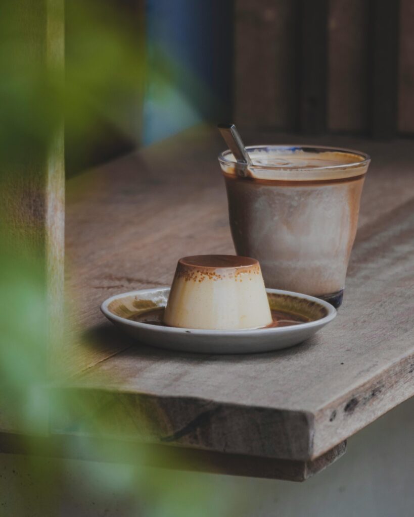 Cup of coffee on a windowsill, with a small upside down cup shaped pastry  